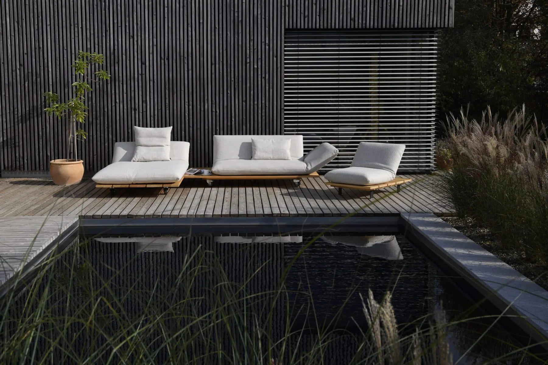 Outdoor-Lounge Akito am Pool vor einer dunklen Holzfassade