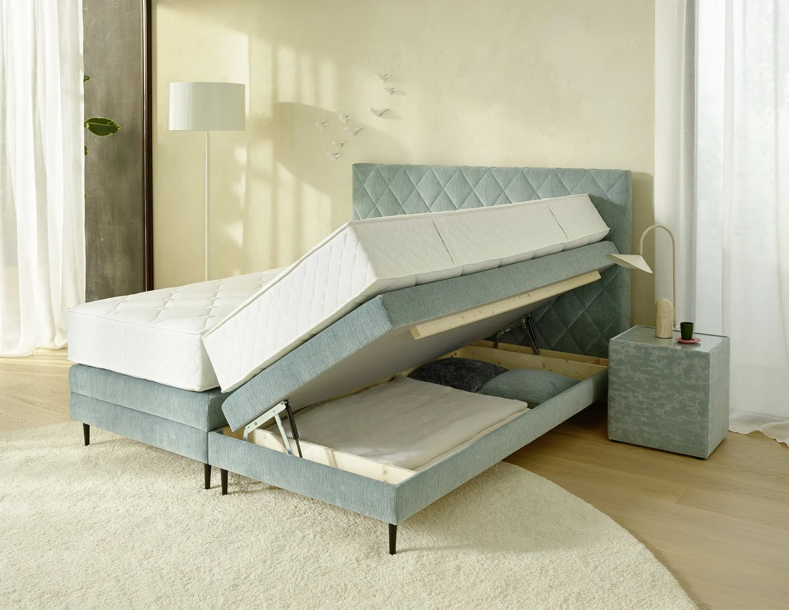 Mintgrünes Boxspringbett mit geöffnetem Bettkasten und angehobenen Liegeflächen