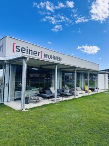 Moderne Fassade des Möbelhauses [seiner] WOHNEN mit gemütlicher Außensitzgruppe